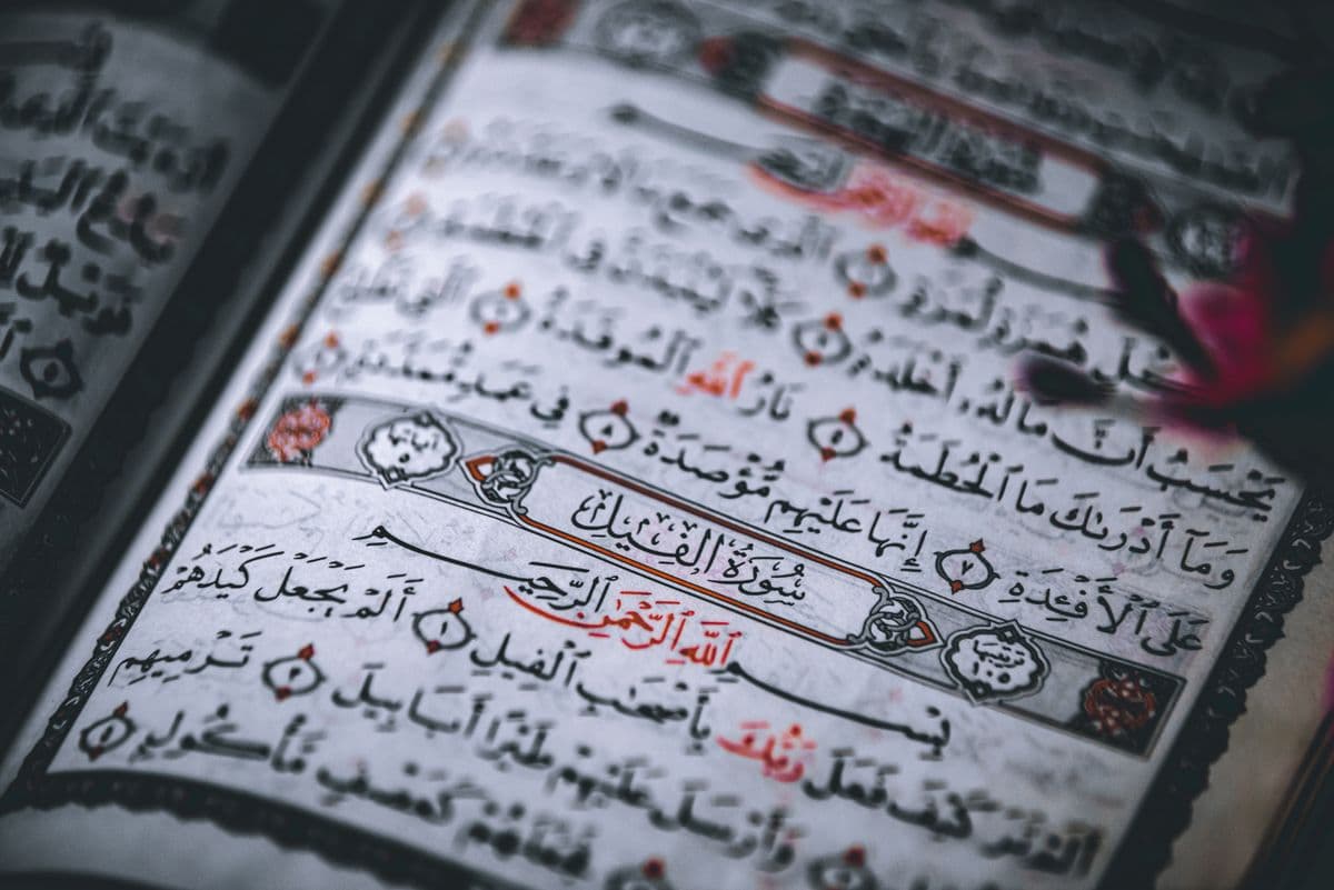 Halaman Al-Quran terbuka yang menampilkan tulisan Arab Surah Al-Fil dengan hiasan kaligrafi.