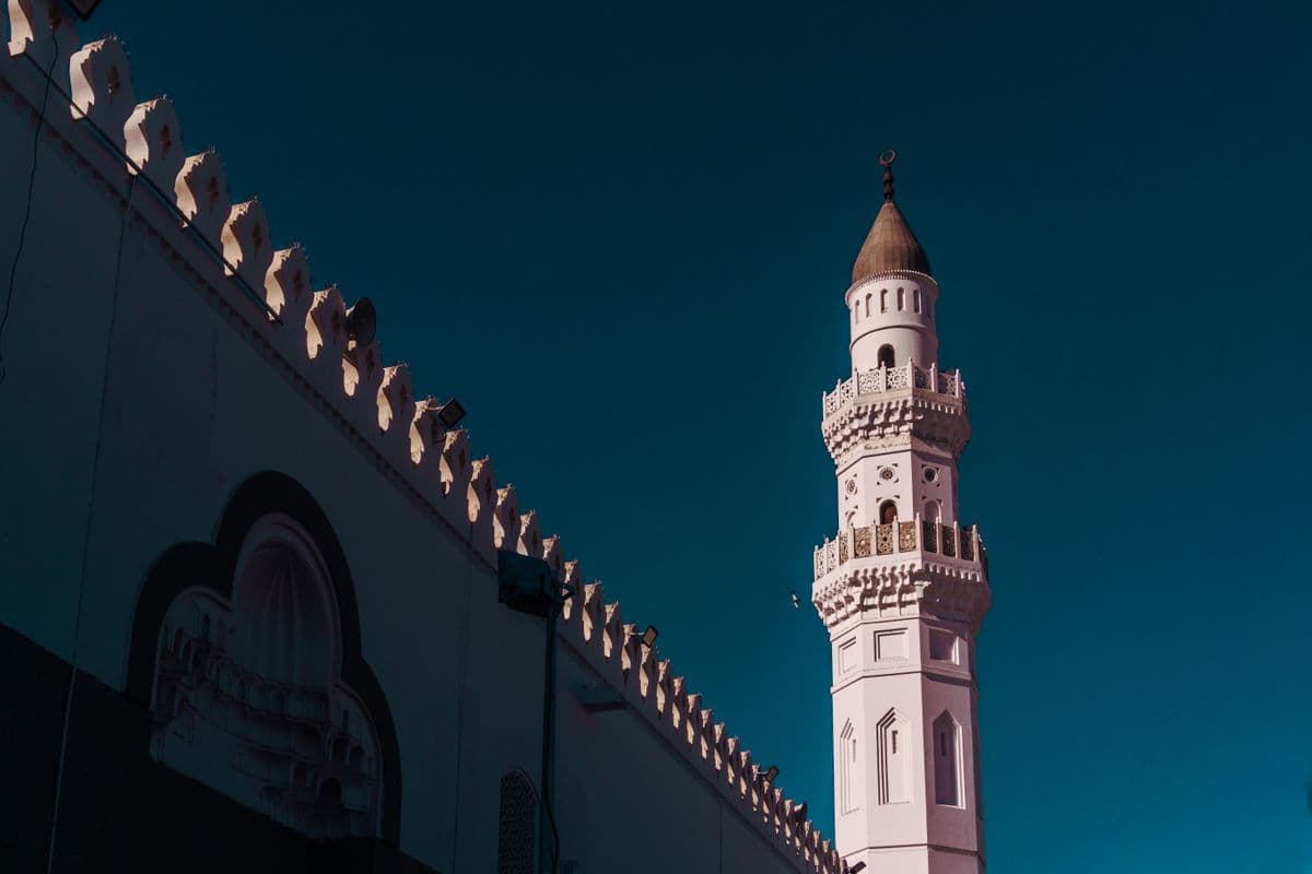 Menara masjid putih dengan detail ukiran indah menjulang tinggi di bawah langit biru cerah.