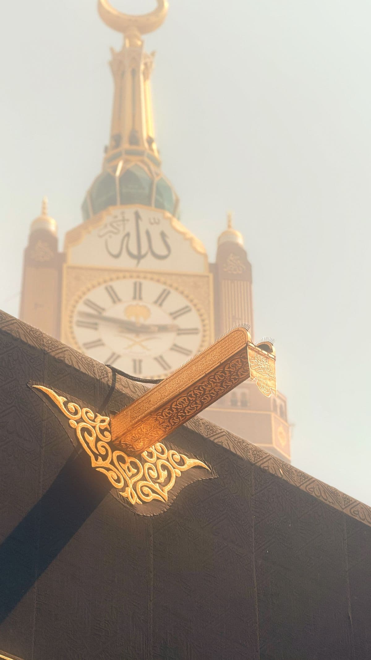 Bagian Multazam Kabah yang dihiasi ornamen emas dengan latar belakang Menara Jam Makkah yang megah.