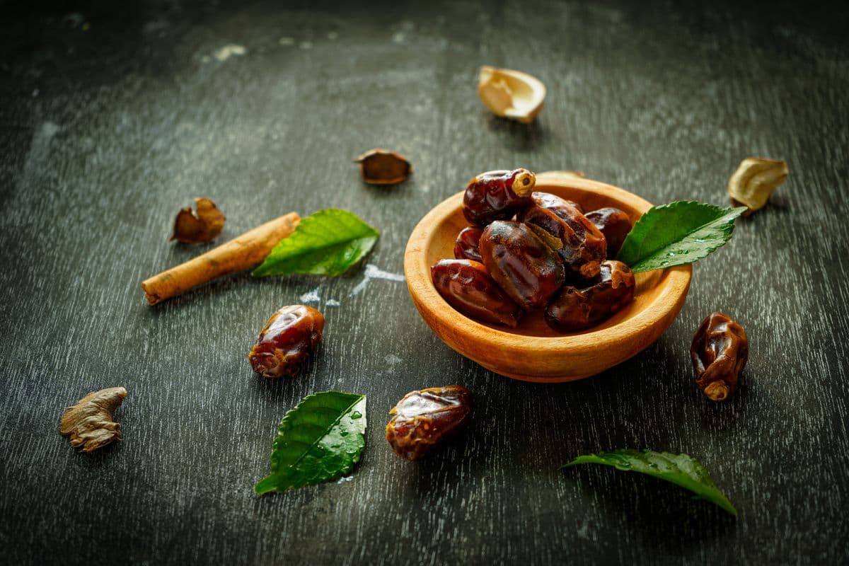 Buah kurma segar dalam mangkuk kayu dan beberapa tersebar di atas meja gelap, cocok untuk oleh-oleh dari Makkah atau Madinah.