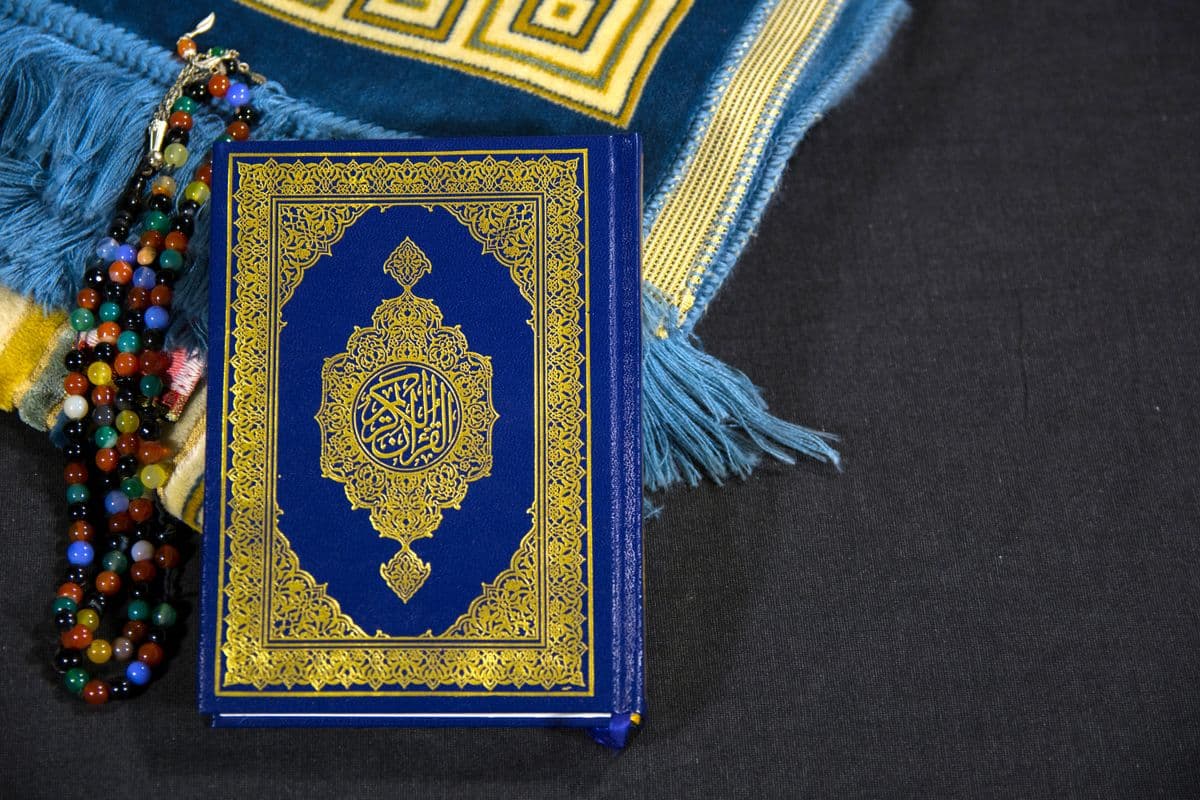 Mushaf Al-Qur'an terbuka berdampingan dengan butiran tasbih di atas sajadah