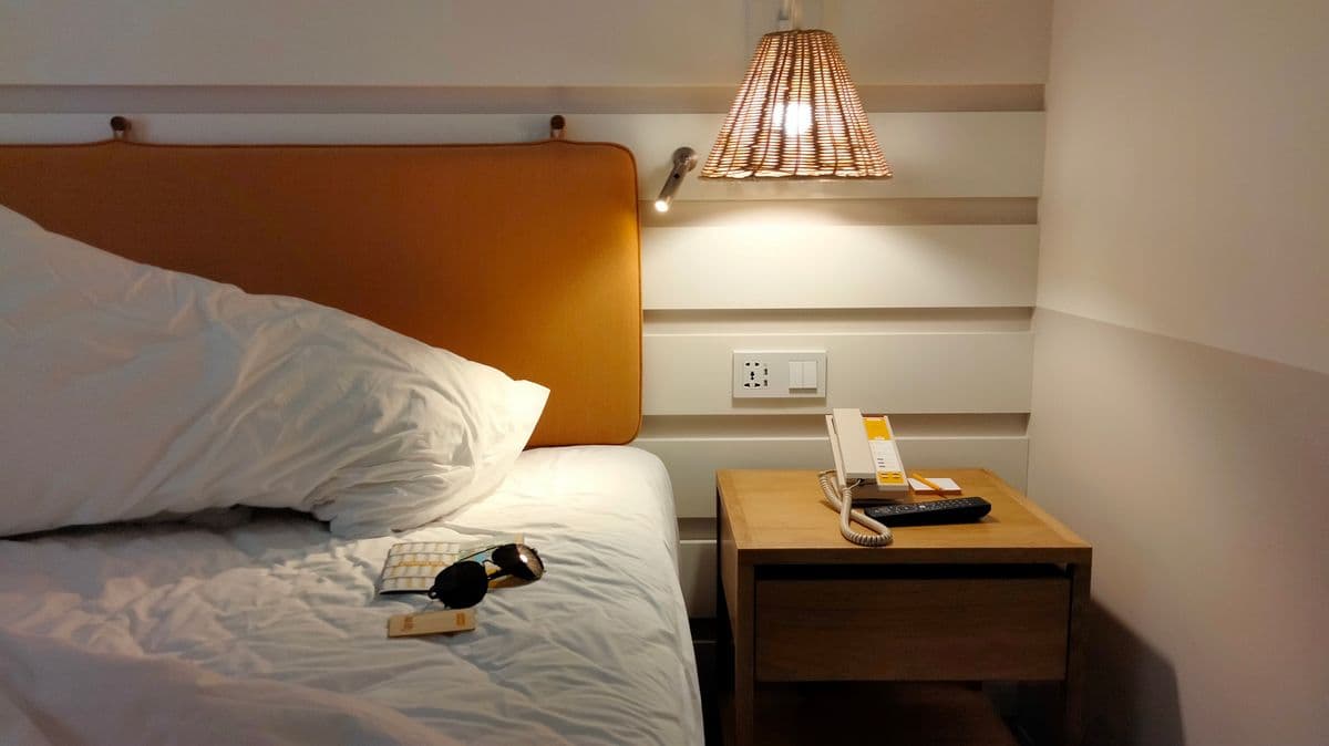 Sudut kamar hotel dengan lampu malam hangat dan kacamata untuk rehat perjalanan