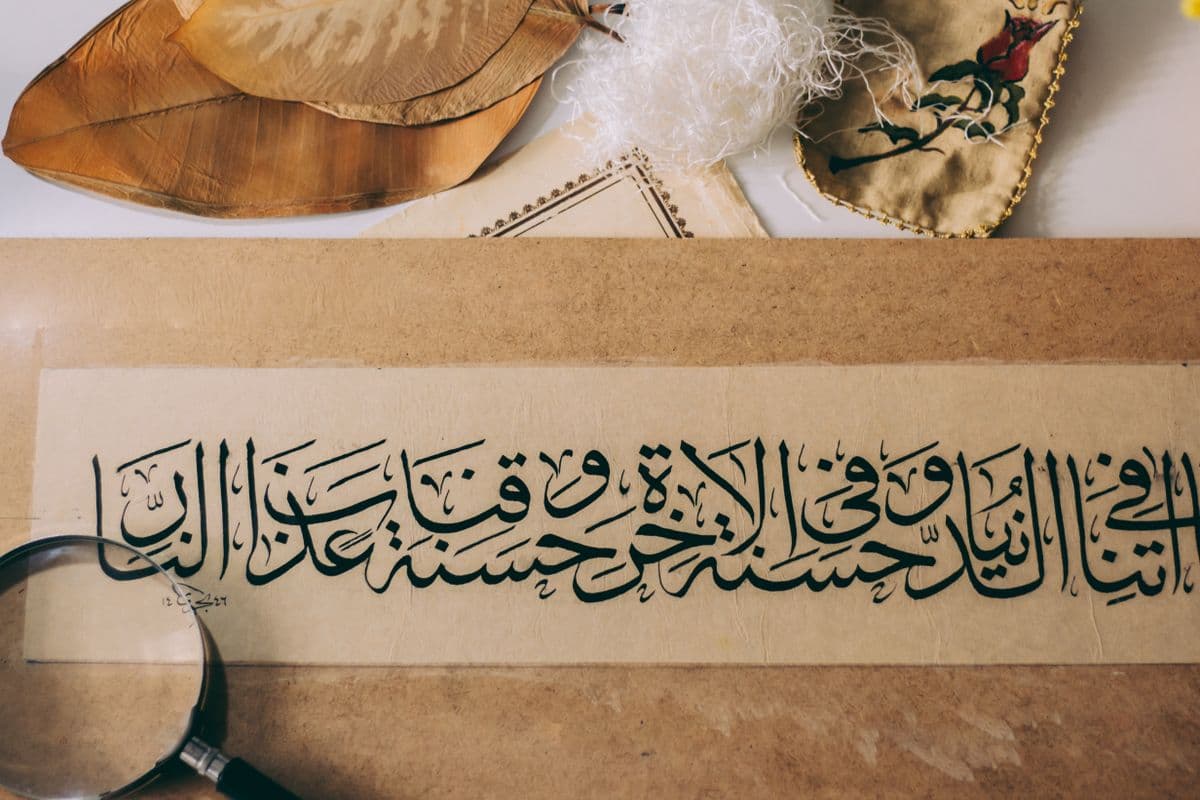 Kertas kaligrafi Arab berisikan ayat suci di atas meja dengan berbagai aksesori.