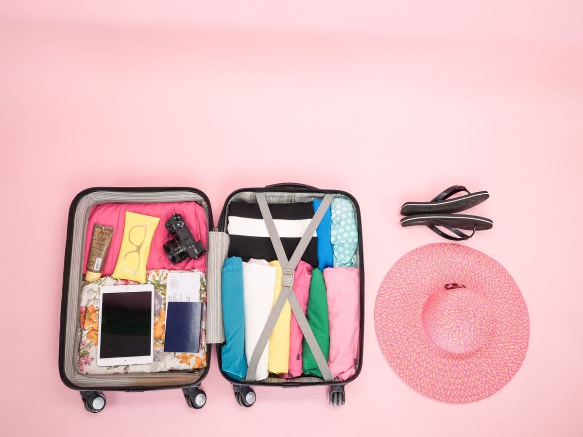 Koper terbuka berisi pakaian, perlengkapan umroh, serta topi pantai pink